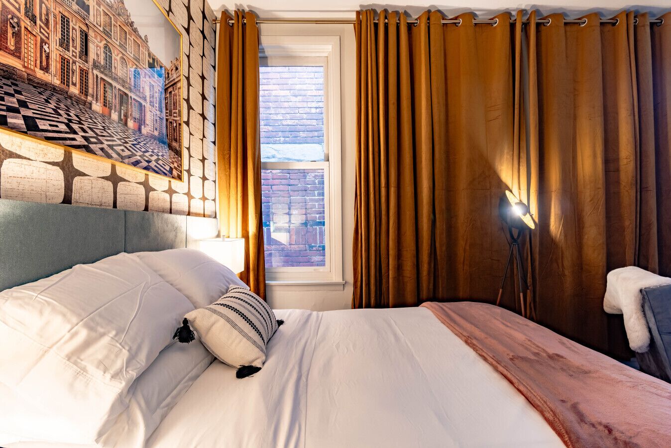 Habitación de hotel con una cama grande, cabecera con diseño geométrico, ventana con cortinas y una lámpara.