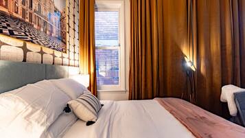 Habitación de hotel con una cama grande, cabecera con diseño geométrico, ventana con cortinas y una lámpara.