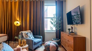 A living room with a sofa, armchair, lamp, TV, and decorative items.