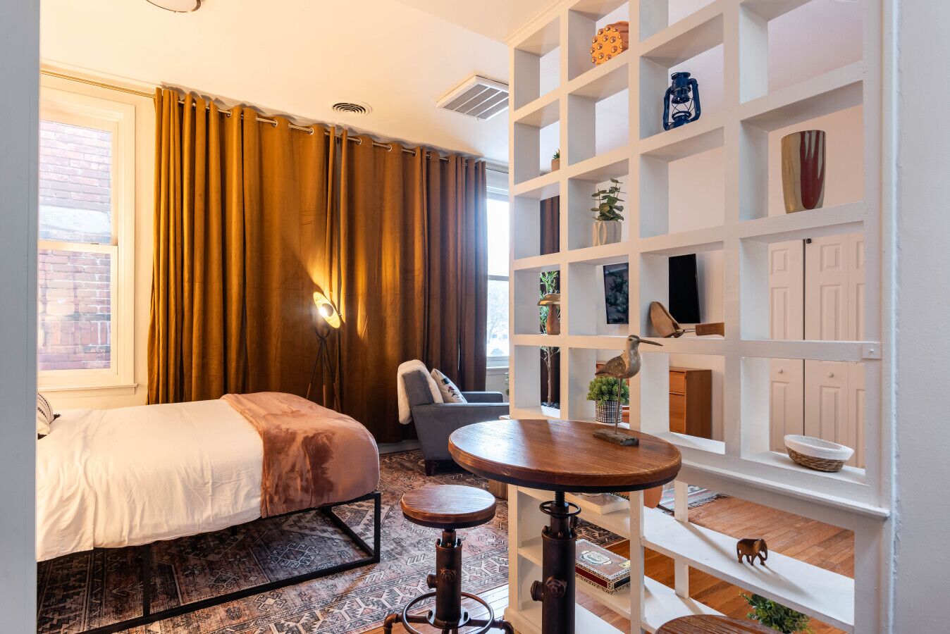 Ein Hotelzimmer mit Bett, Schreibtisch, Stuhl, Bücherregal und einem Fenster mit Vorhängen.