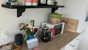 Eine Küche mit weißen Schränken, einer Holz Arbeitsplatte und einer Mikrowelle. Auf der Arbeitsplatte befinden sich verschiedene Küchenutensilien, darunter ein Wasserkocher, eine Kaffeemaschine und ein Korb.