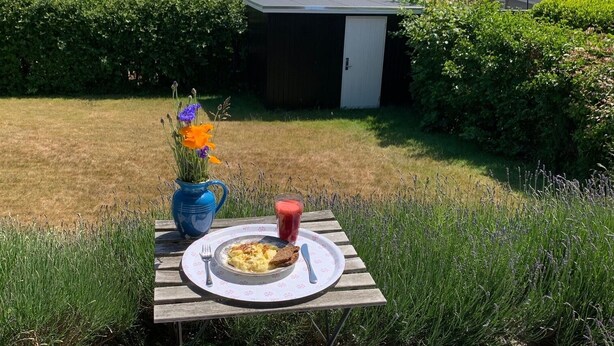 Eine Terrasse mit Frühstückstisch, eine kleine Gartenhütte und Blick auf das Meer.
