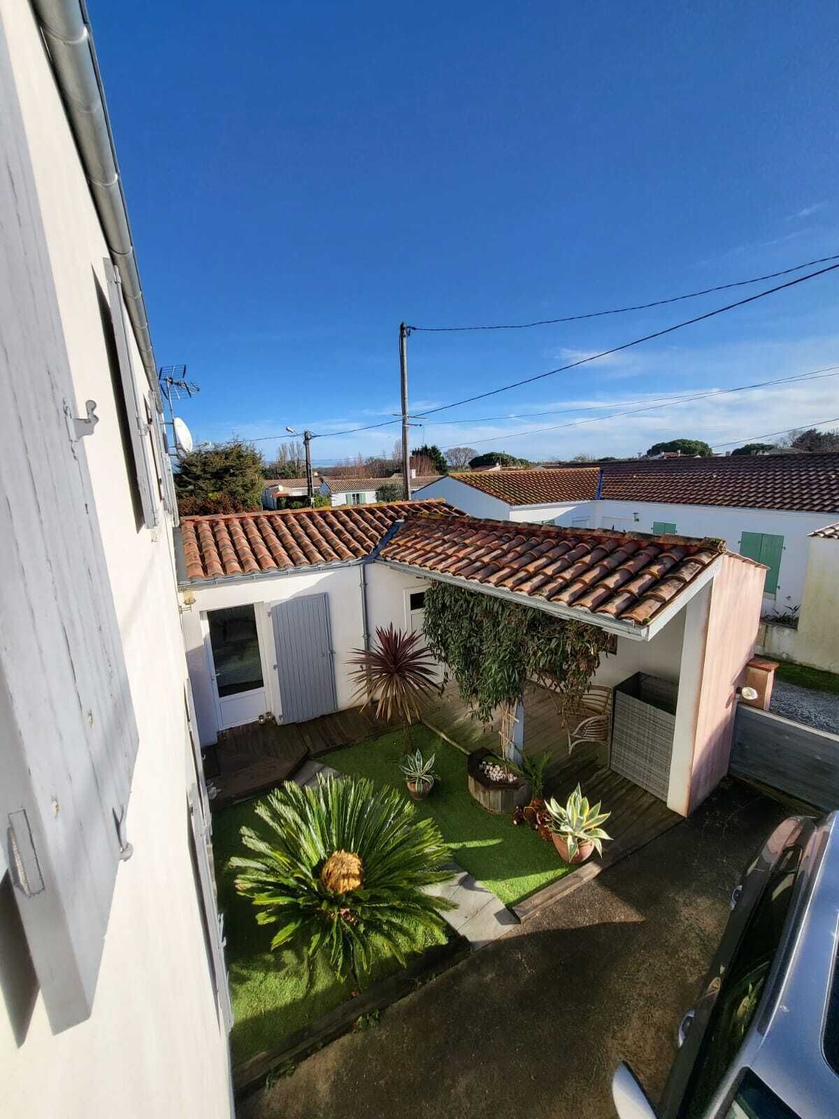 Un quartier résidentiel avec des toits recouverts de tuiles en terre cuite, un petit jardin agrémenté de palmiers et un bâtiment blanc doté d’un garage.