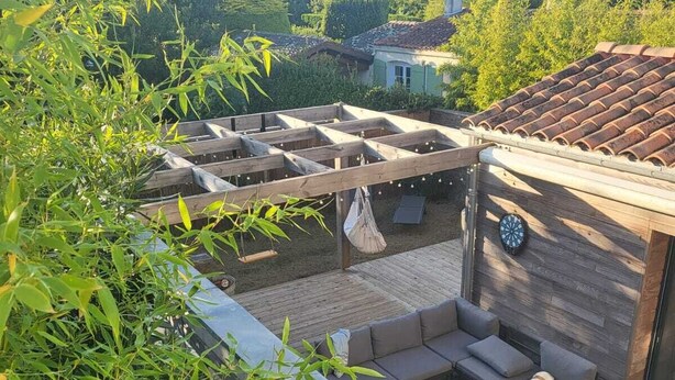 Un patio exterior techado con cubierta de madera, un rincón de estar con cojines y un dardo.