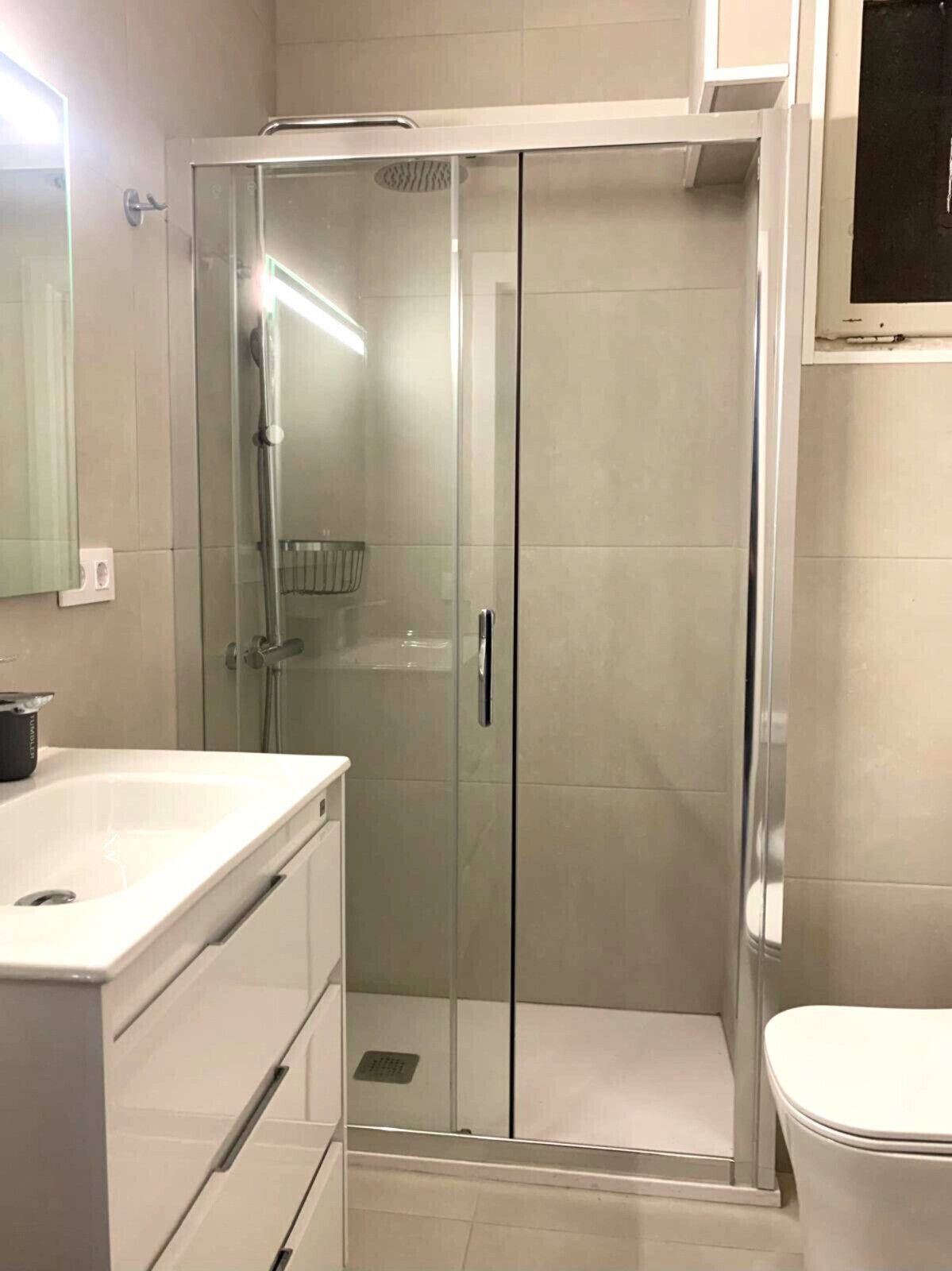 A modern bathroom with a glass-enclosed shower, a white sink, and a toilet.