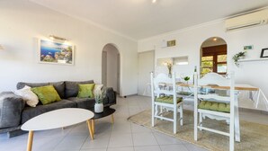 A living room with a grey sofa, a white coffee table, and a dining area with a white table and chairs. - EDEN MAR 1A Roses (Rosas / Roses)