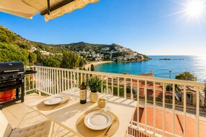 Varanda com mesa posta para dois, com vista para a costa, casas e praia.