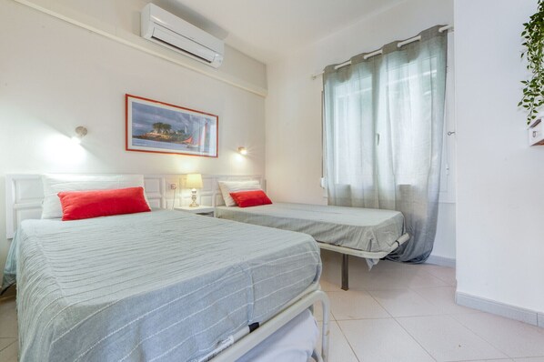 A hotel room with two beds, a painting, an air conditioner, and a window with curtains. - EDEN MAR 1A Roses (Rosas / Roses)