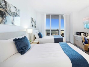 Quarto de hotel com duas camas, uma escrivaninha, televisão e uma grande janela com vista para a cidade.