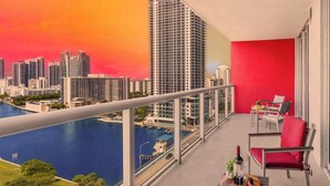 A balcony with a city view, a table with a bottle and glass, and red chairs.