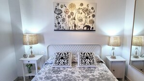 Un dormitorio con cama, dos mesitas de noche, dos lámparas, un espejo y un cuadro en la pared.