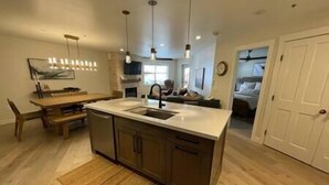A modern kitchen with a central island, wooden dining table, and pendant lighting. - NEW!  Deluxe Ski In/Out 2B/2B condo at Solitude (Brighton)