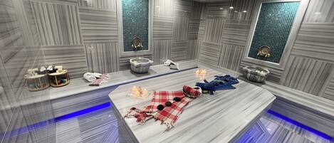 A spa room with a marble floor, a massage table, a small pool, and a window with a view.