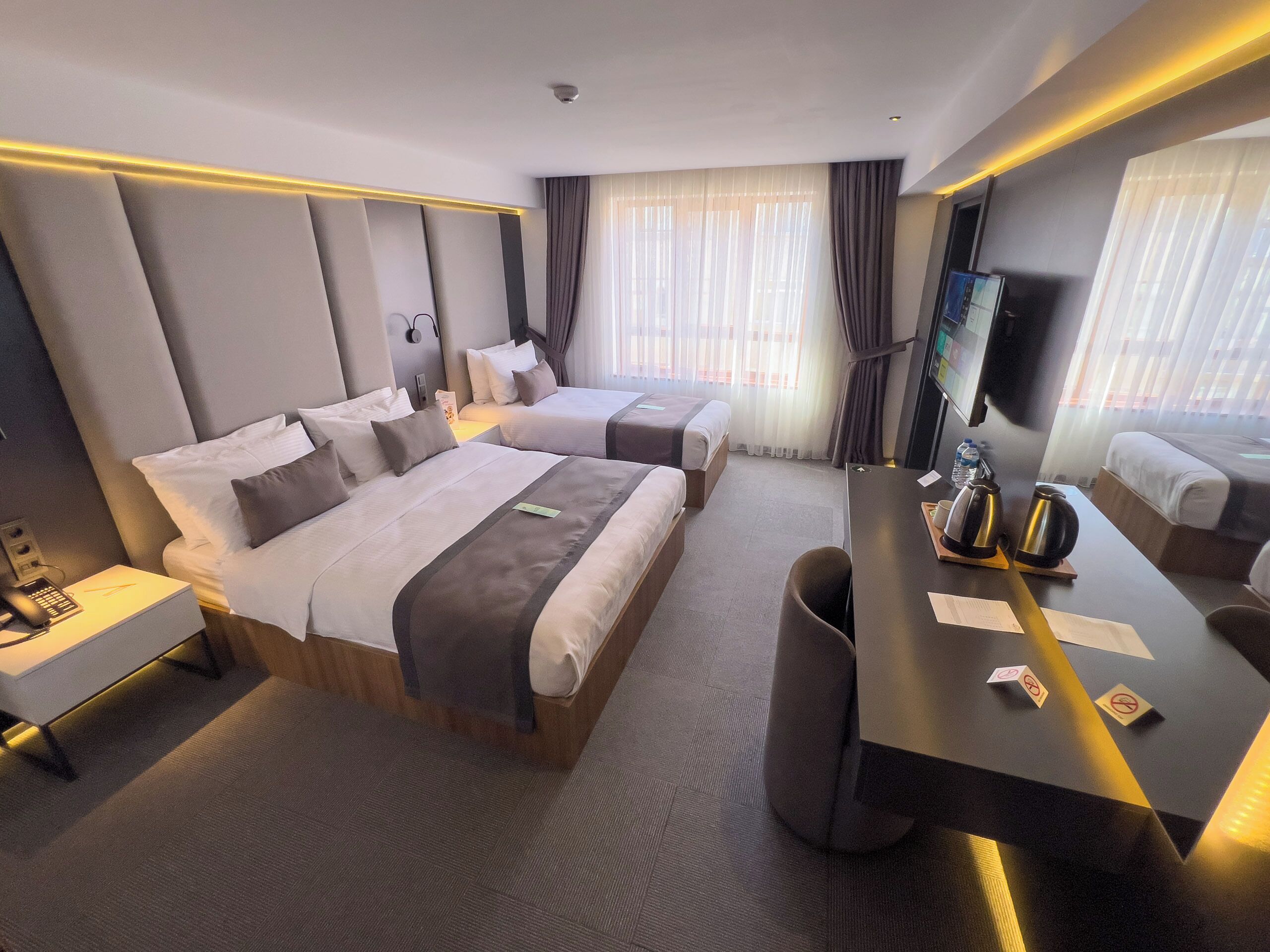 A hotel room with two beds, a desk with a coffee maker, a TV, and a bathroom with a shower and toilet.