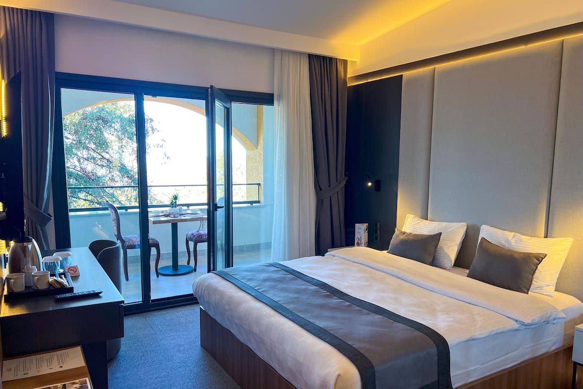 A hotel room with a large bed, a desk with a coffee maker, and a view of the outdoors through a sliding door.