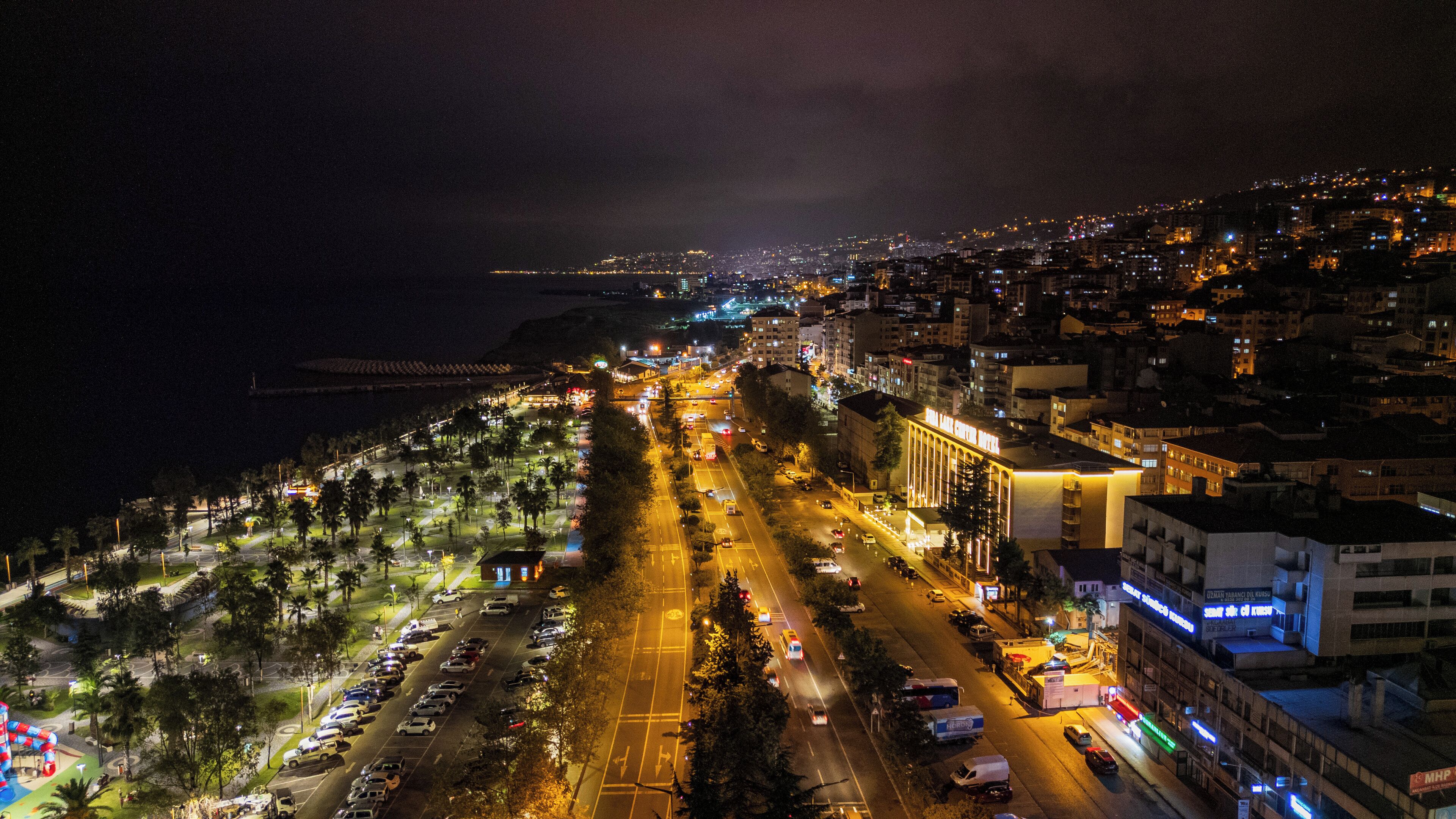 Une vue aérienne nocturne d’une ville côtière, avec une large route, des bâtiments et une plage.