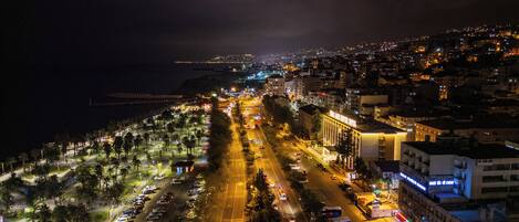 Une vue aérienne nocturne d’une ville côtière, avec une large route, des bâtiments et une plage.