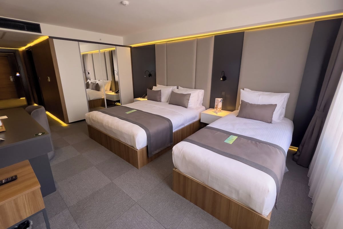 A hotel room with two beds, a desk, and a mirror.