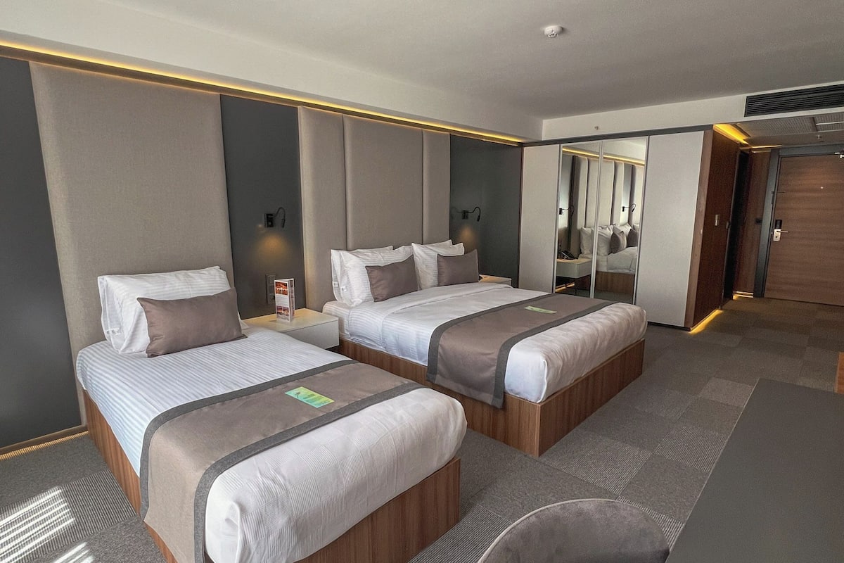 A hotel room with two beds, a desk, and a mirror.