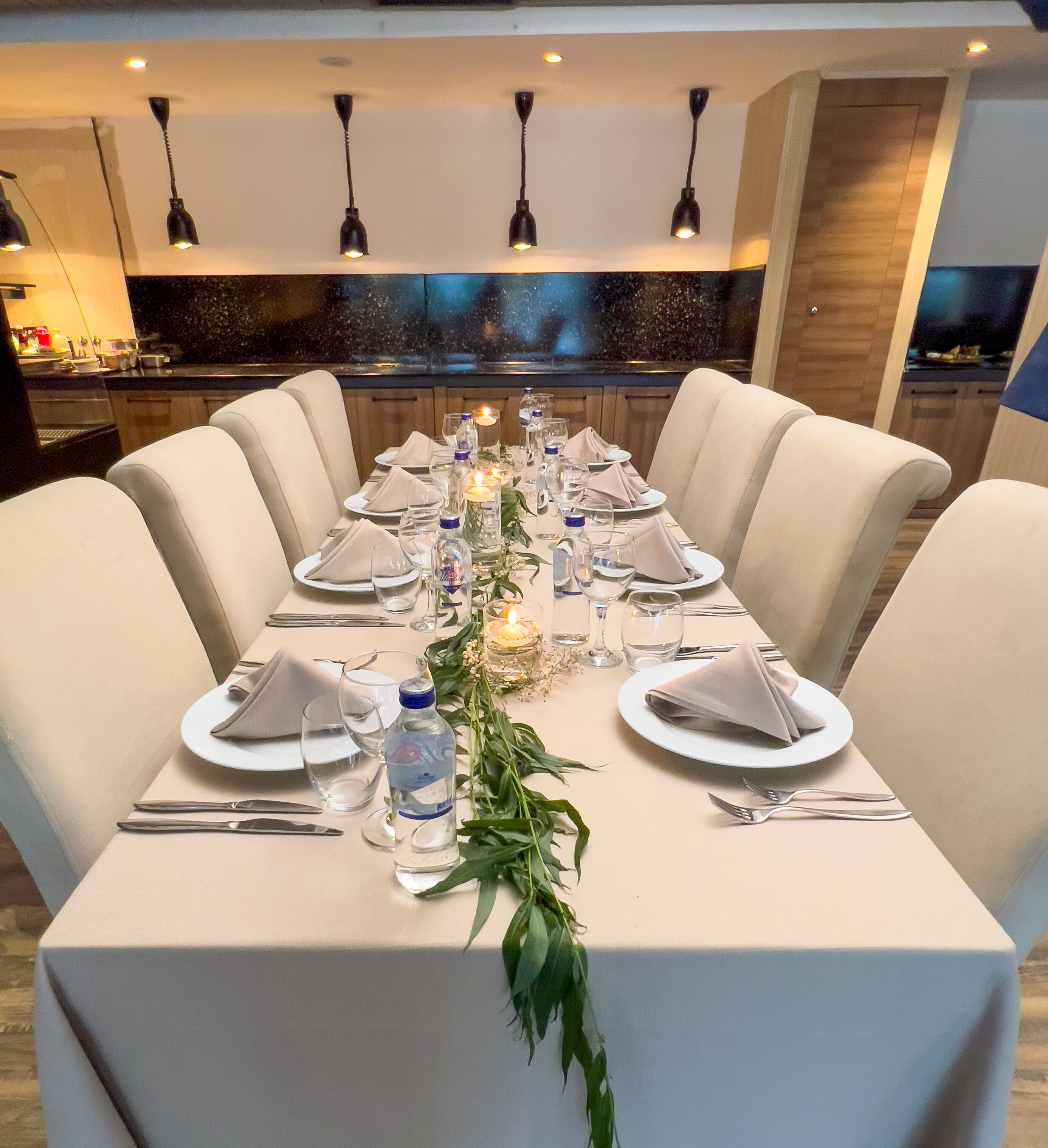 A long dining table set for a meal with white tablecloths, plates, and cutlery.