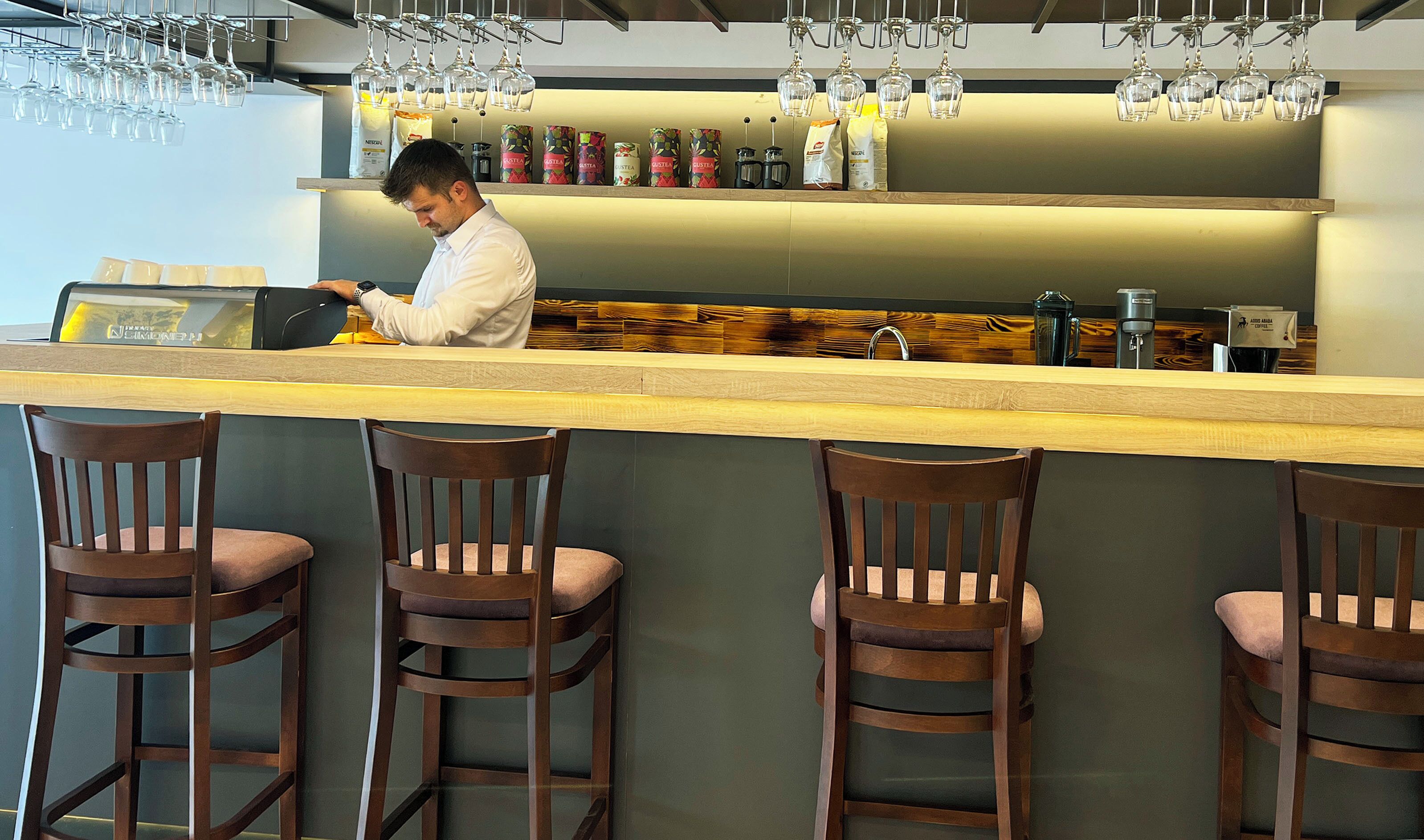 A bar area with wooden chairs, a counter, and hanging wine glasses.