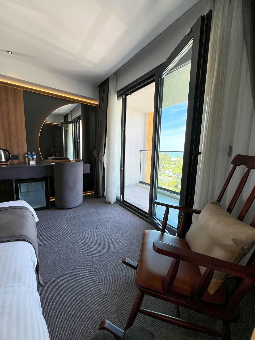 Ein Hotelzimmer mit Bett, Schreibtisch mit Stuhl, großem Fenster mit Aussicht und einem Holzstuhl.