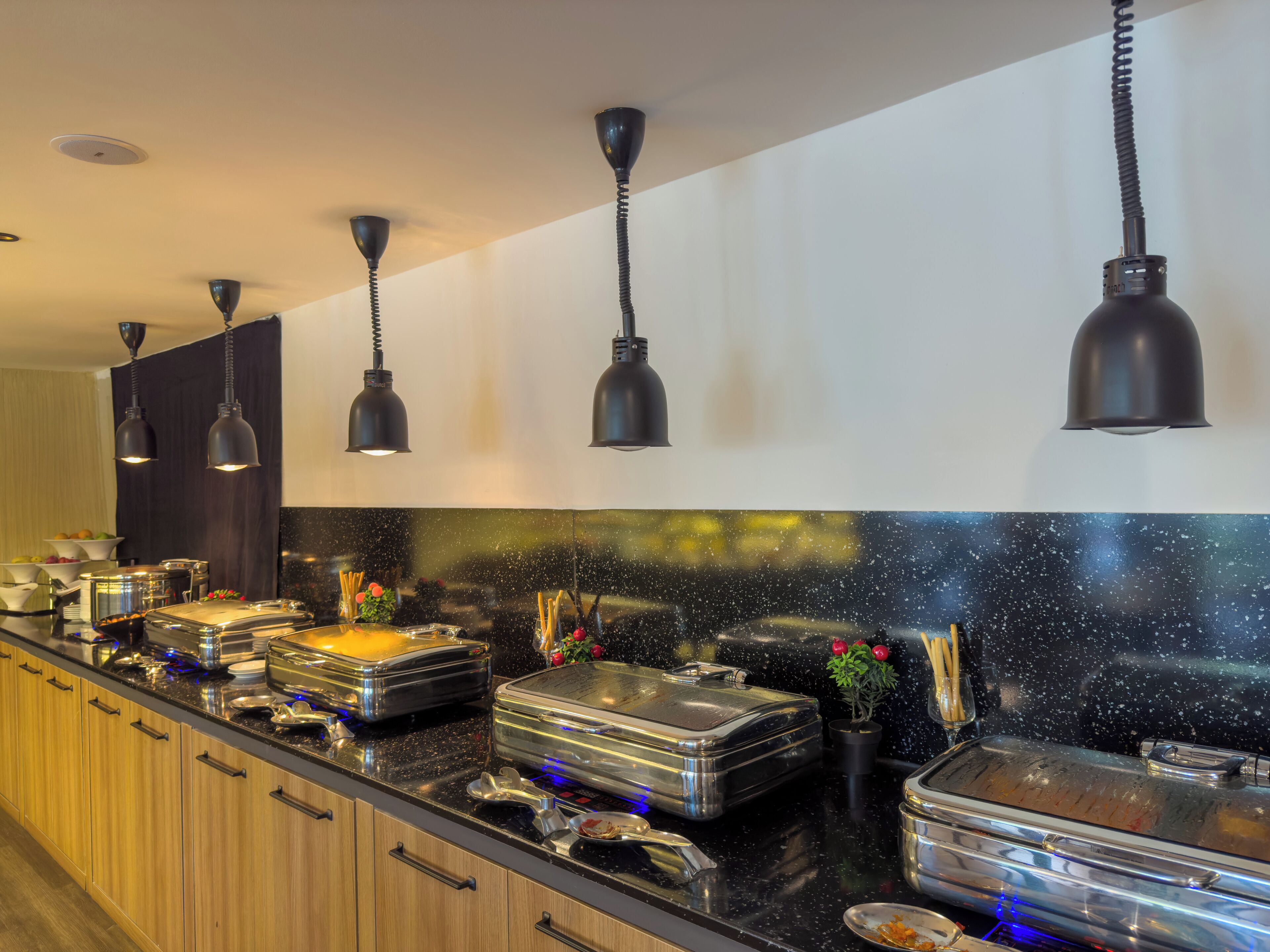 A modern kitchen with black pendant lights, stainless steel appliances, and a black countertop.