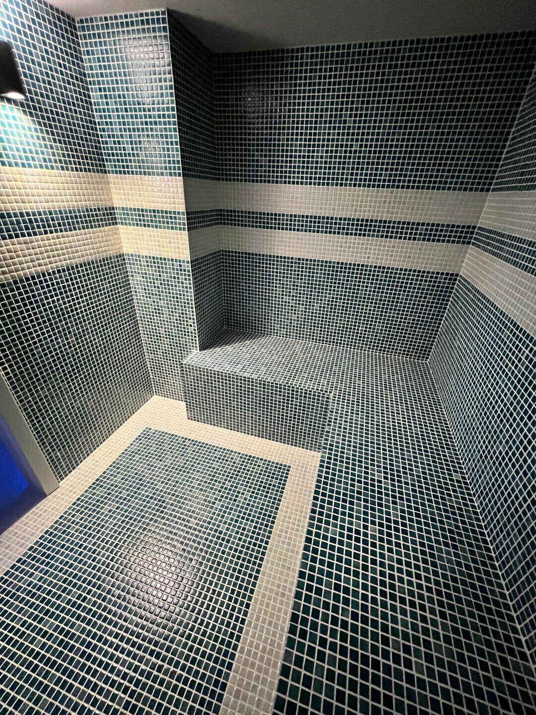 A bathroom with a tiled floor and walls, featuring a corner sink and a mirror.