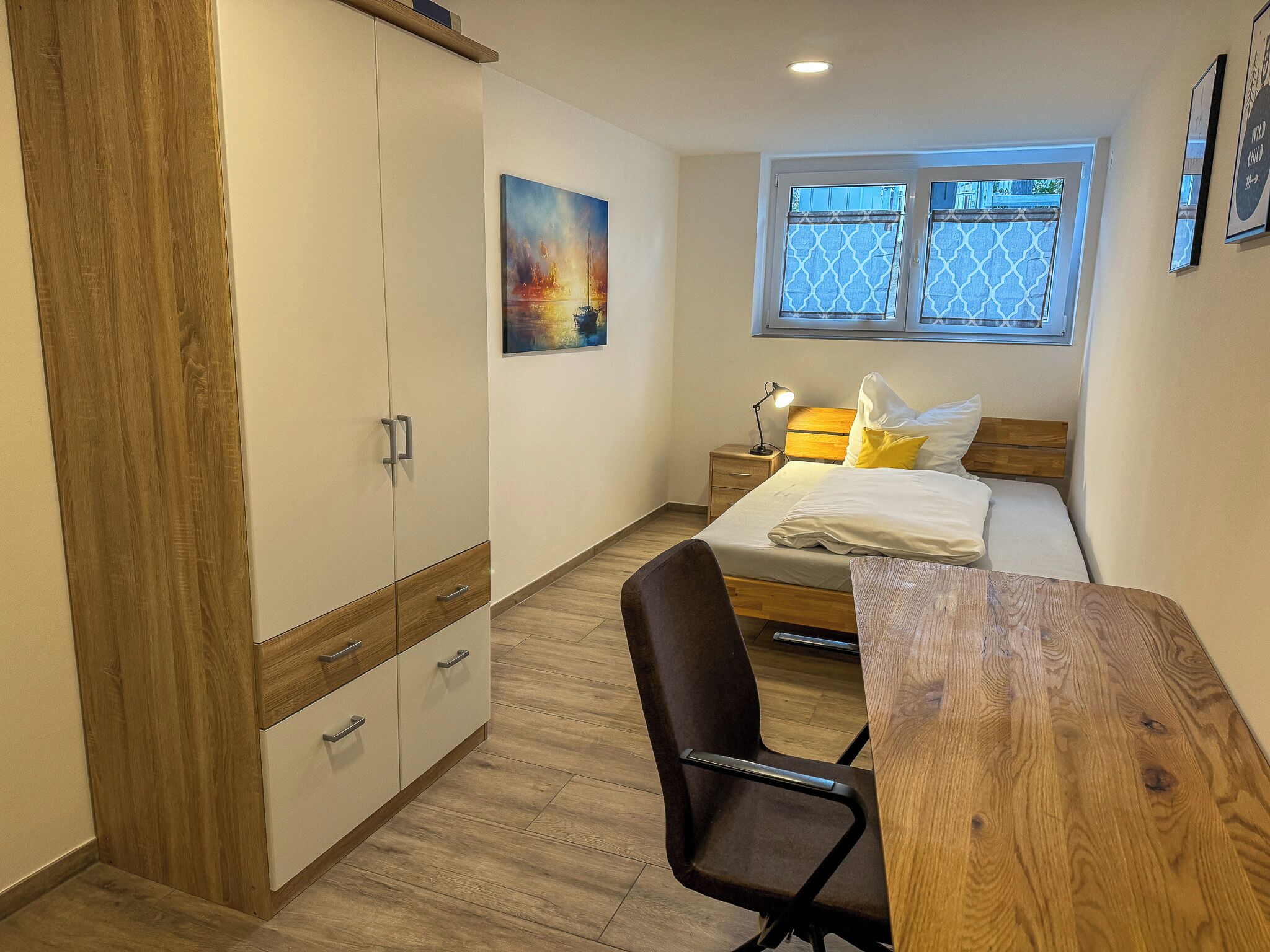 Une chambre à coucher comprenant un lit, un bureau, une chaise, une armoire, une table de chevet et une fenêtre.