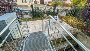 Zona residencial con una escalera metálica que conduce a una entrada portonada, rodeada de casas con techos de tejas rojas y un área verde con árboles.
