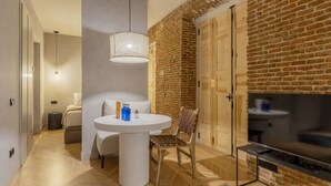A modern living room with a brick wall, a TV, a dining table with chairs, and a sofa. - w *| Luxury 1BR at Palacio Real (Madrid)