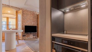 A modern kitchen with a built-in oven, a flat-screen TV, and a brick wall. - w *| Luxury 1BR at Palacio Real (Madrid)
