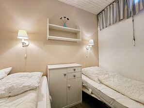 Two single beds with white duvets and pillows, a shelf unit with a vase, and wall-mounted lamps.