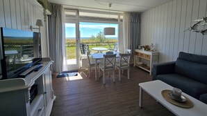 Un salon comprenant un téléviseur, un canapé, une table à manger avec des chaises, et donnant sur l’extérieur.