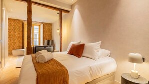 A modern bedroom with a large bed, a wooden beam ceiling, a brick wall, and a small bedside table with a lamp. - w *| Amazing 1BR at Palacio Real (Madrid)