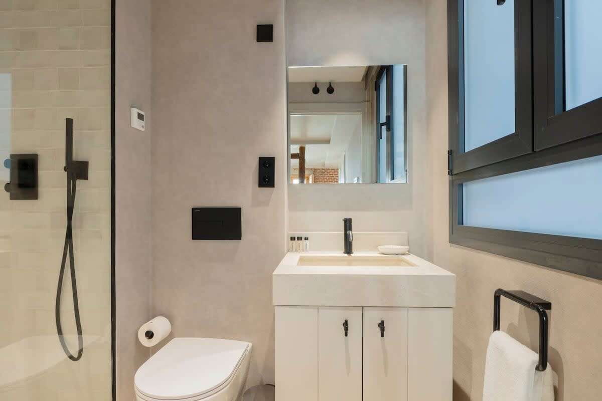 Un baño moderno con cabina de ducha de vidrio, inodoro, tocador con almacenamiento y espejo sobre el lavabo.