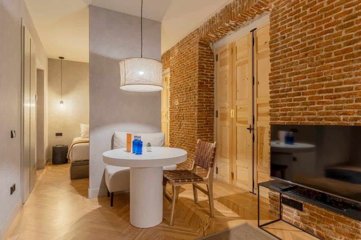 Un salon moderne avec un mur en briques, une table ronde blanche, un canapé et un téléviseur.
