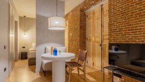 A modern living room with a brick wall, a round white table, a sofa, and a TV. - w * | Modern 1BR at Palacio Real (Madrid)
