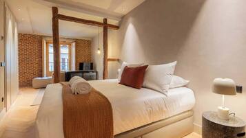Une chambre d’hôtel moderne avec un grand lit, une poutre en bois au plafond, un mur en briques et un petit bureau avec une lampe.
