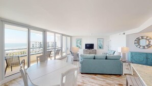 Ein großzügiger Wohnbereich mit Balkon und Meerblick, inklusive einer Couch, einem Esstisch und einem Fernseher.
