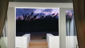 Habitació amb una finestra gran que mostra un paisatge natural amb gespa i arbres. Hi ha dues cadires blanques davant la finestra.