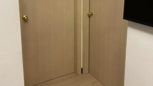 Una habitación con puerta de madera, un televisor negro montado en la pared y piso de color claro.