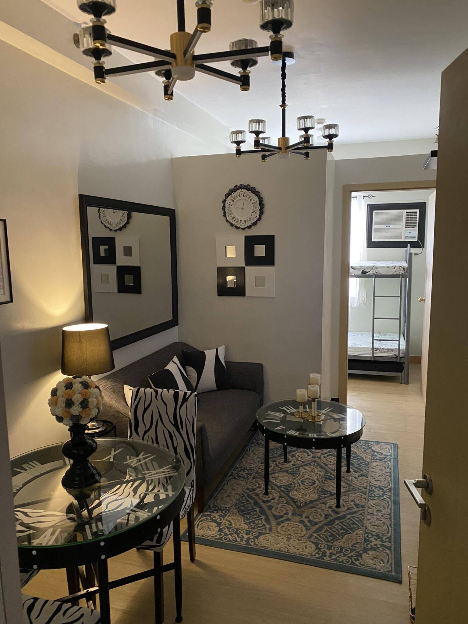 Ein Wohnzimmer mit einer Couch, einem Glastisch mit einem zebra-gemusterten Sessel, einem runden Couchtisch mit Kerzen, einer Chandelierleuchtre und einer Wanduhr.