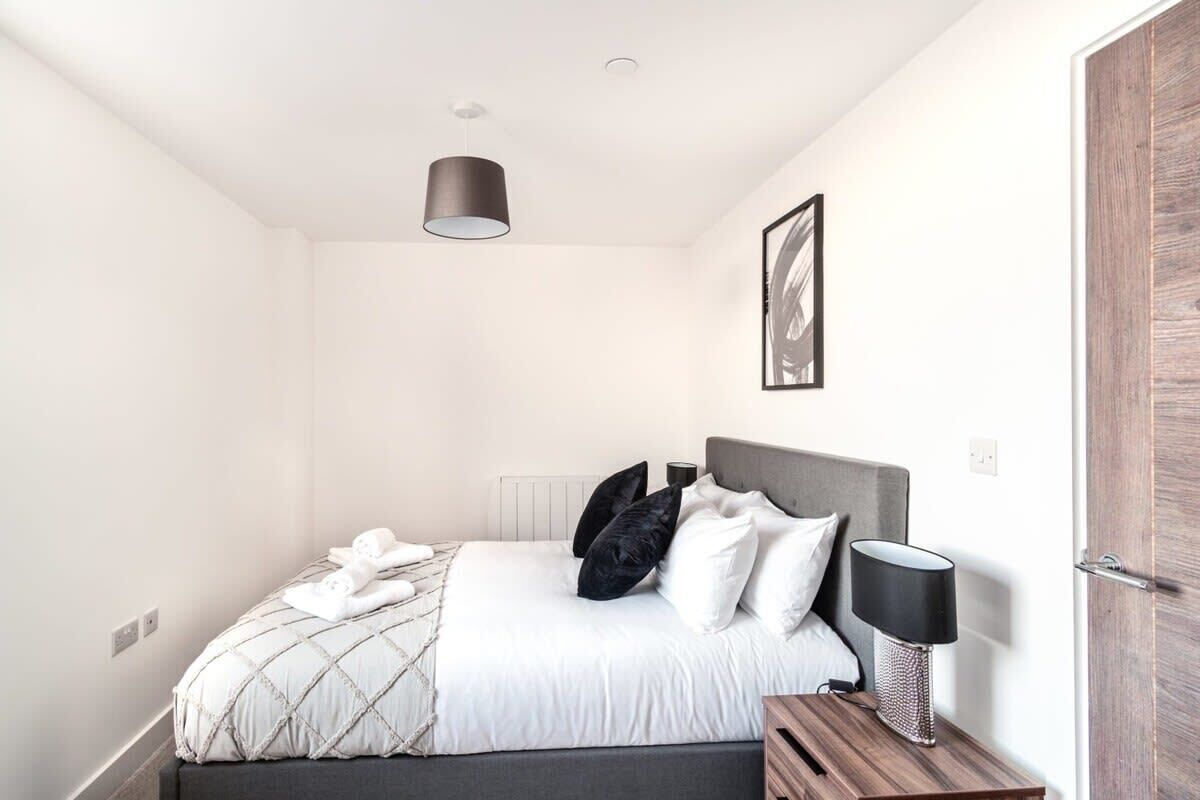 A bedroom with a bed, bedside table, lamp, and a framed picture on the wall.