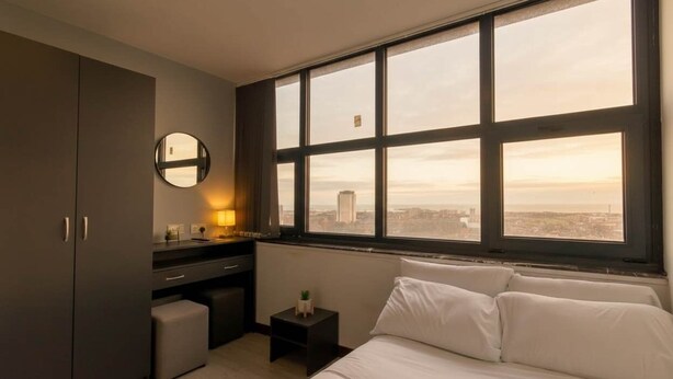 A modern bedroom with a large window, a desk, and a bed. - Convenient Budget Sunderland Studio with Views (Sunderland)