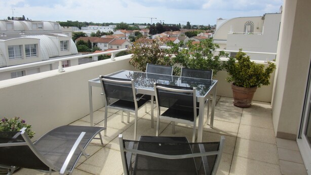 Ein Balkon mit Glastisch und Stühlen, einem Blumentopf und Blick auf Gebäude in der Ferne.