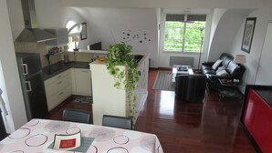Eine moderne Küche mit Kochinsel, Essbereich mit Tisch und Stühlen, ein Wohnzimmer mit Sofa und Couchtisch sowie ein großes Fenster für natürliches Licht.