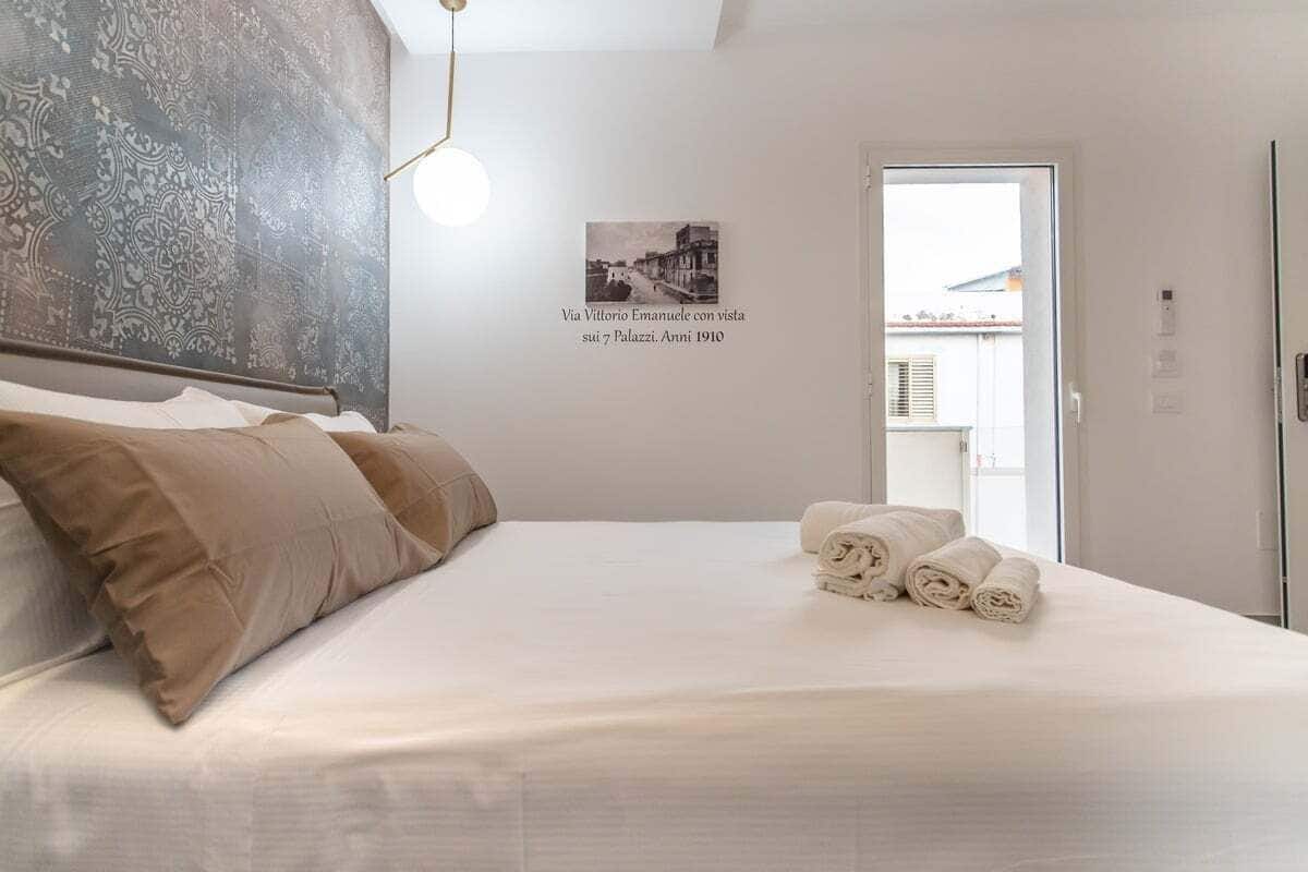Une chambre d’hôtel avec un lit, des oreillers, un tableau accroché au mur et une porte donnant sur un balcon.