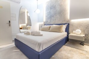A modern bedroom with a large bed, a bedside table, a nightstand, and a wall-mounted mirror. - azzurra guest house  (Lampedusa)