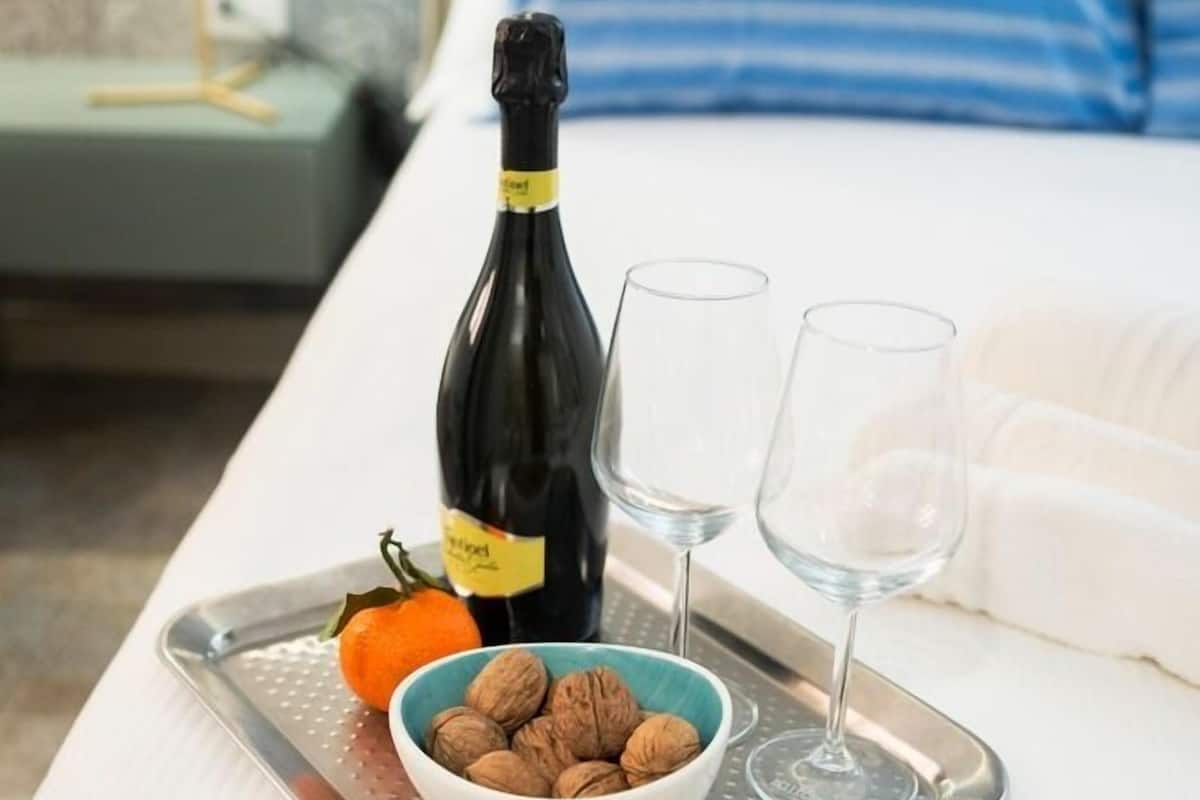 Un lit avec un plateau contenant une bouteille de vin, deux verres, un bol de noix et une orange.